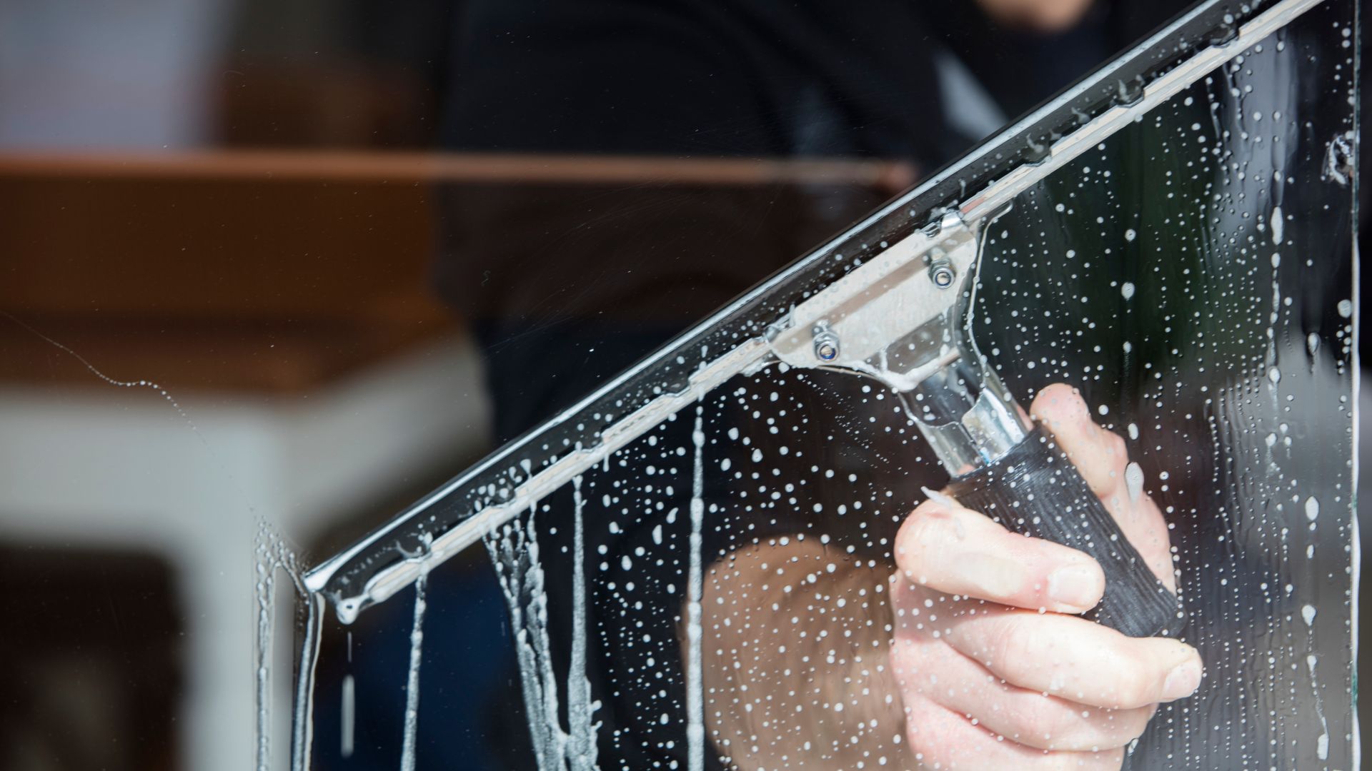 Hand cleaning wet window with squeegee, water droplets visible