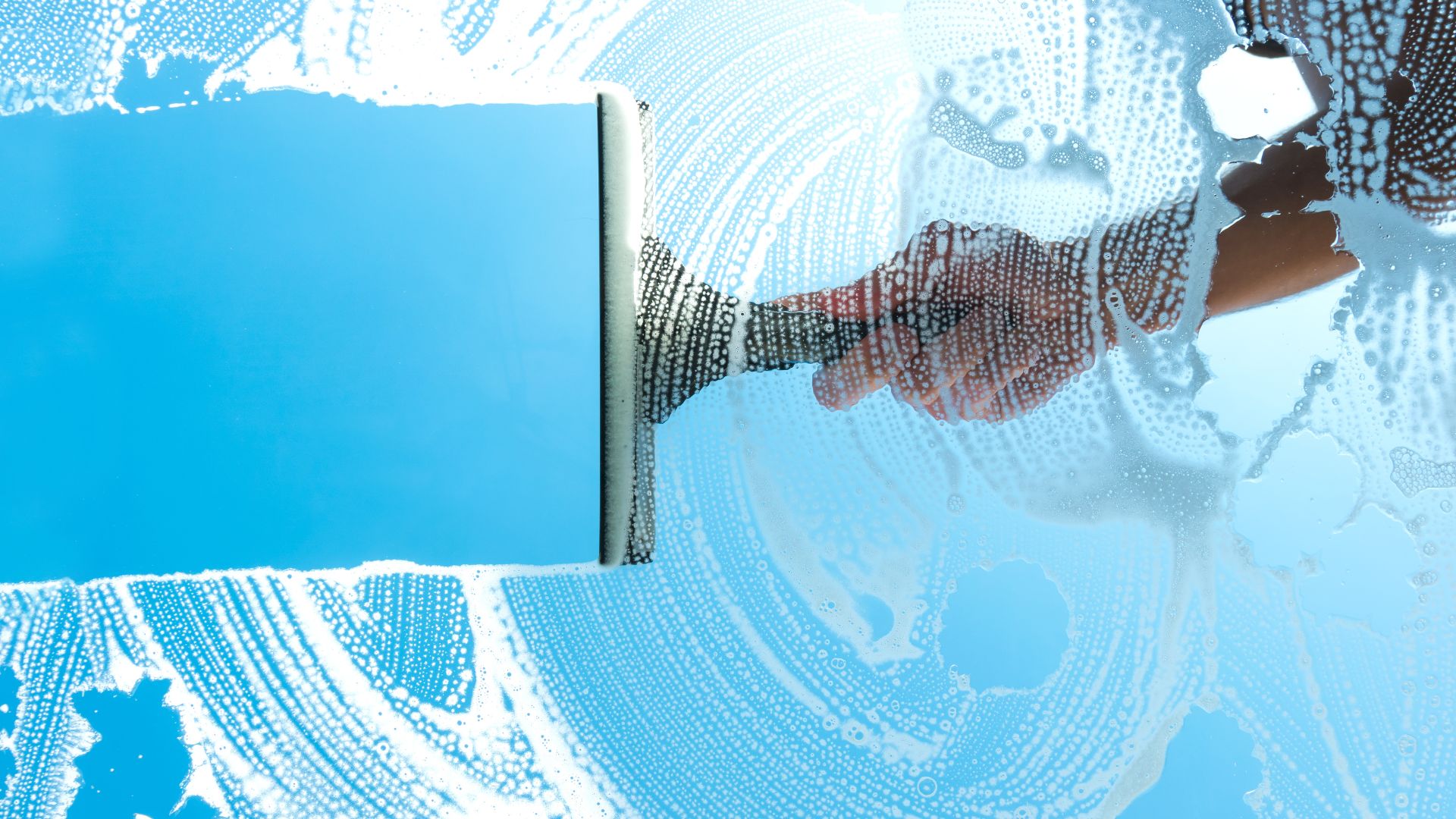 Window squeegee cleaning wet glass with blue and white droplets