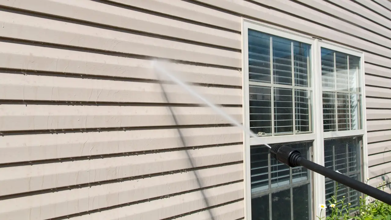 Pressure washing dirt and grime from a home's siding beside a window